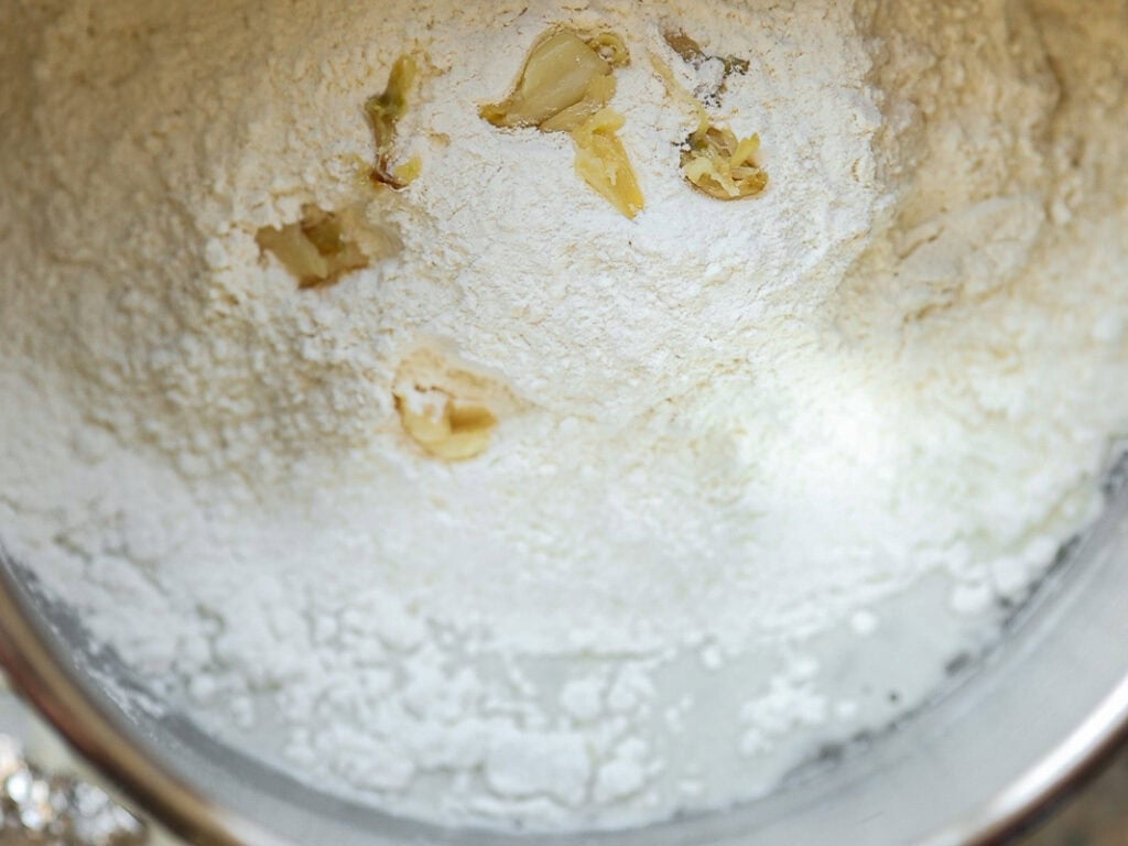 A metal mixing bowl filled with white flour and roasted garlic. The ingredients are ready to be mixed for baking.